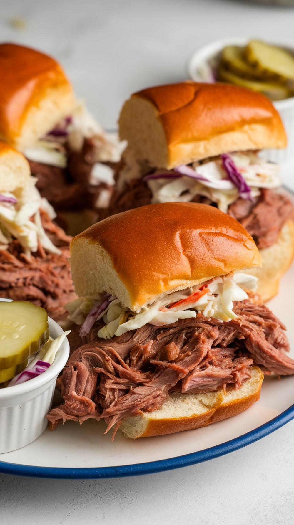BBQ Chuck Roast Sliders on a plate with pickles and coleslaw.